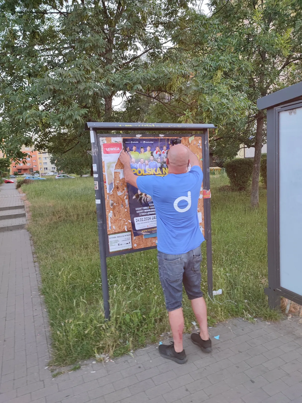 Naklejanie plakatu na tablicy ogłoszeń przy chodniku