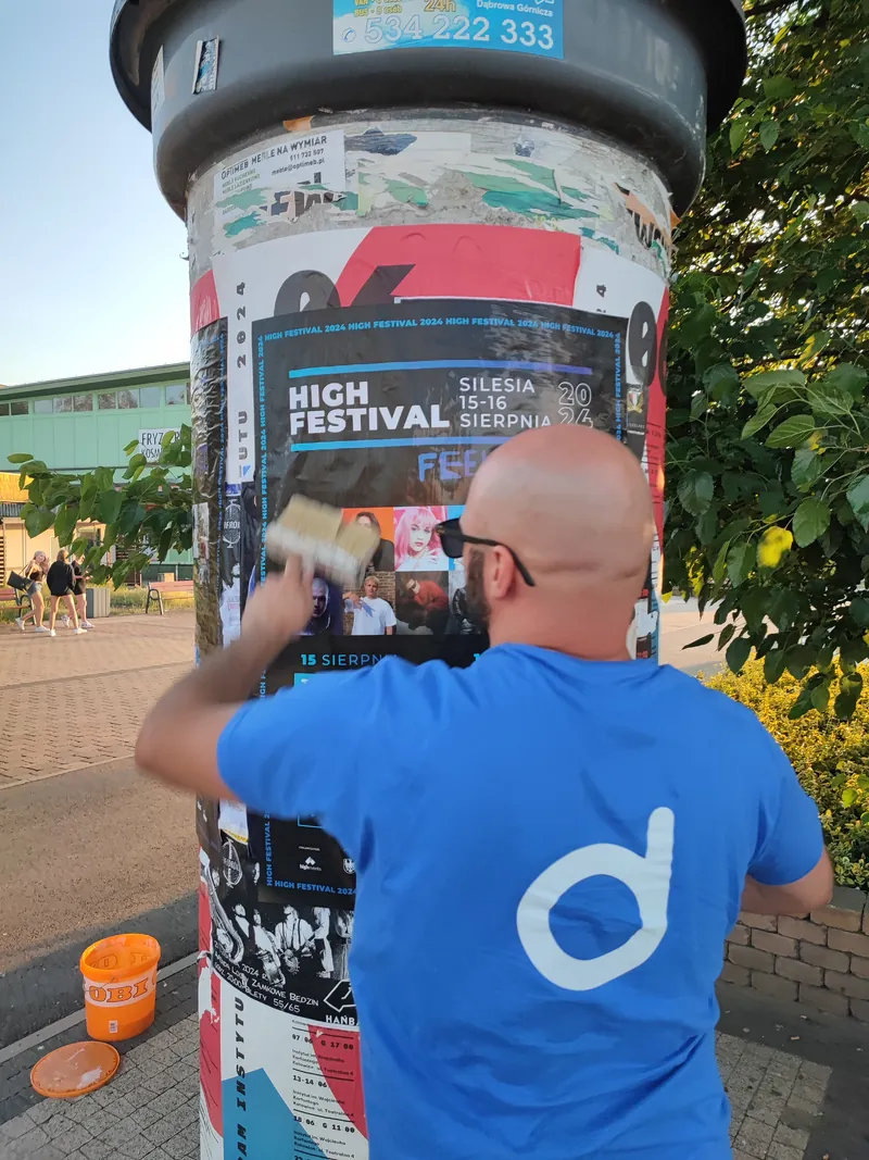 Dociskanie plakatu pędzlem na słupie ogłoszeniowym