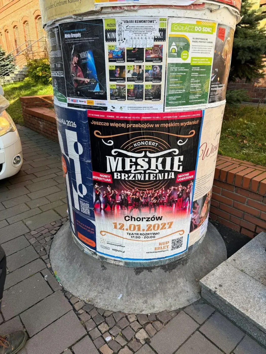 Plakat Męskie Brzmienia na słupie ogłoszeniowym przy ceglanej zabudowie w Chorzowie