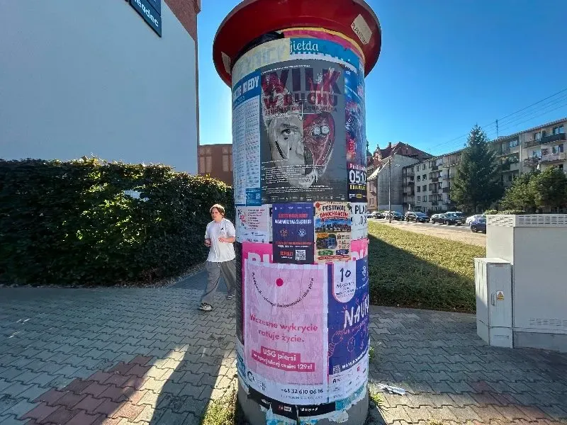Różowy plakat badań USG piersi na słupie ogłoszeniowym wśród innych plakatów