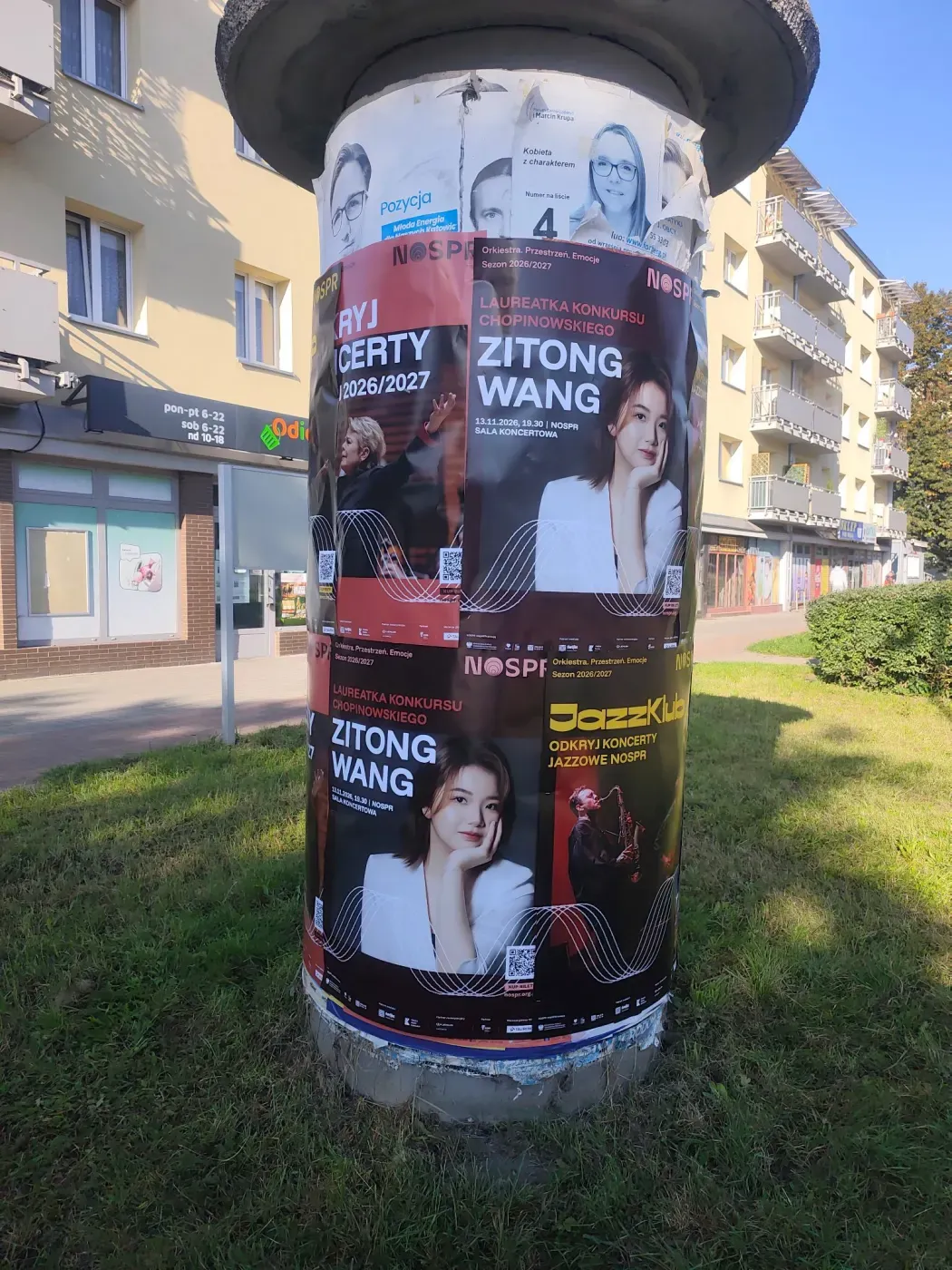 Słup ogłoszeniowy pod blokami z plakatami Zitong Wang, Odkryj koncerty i JazzKlub