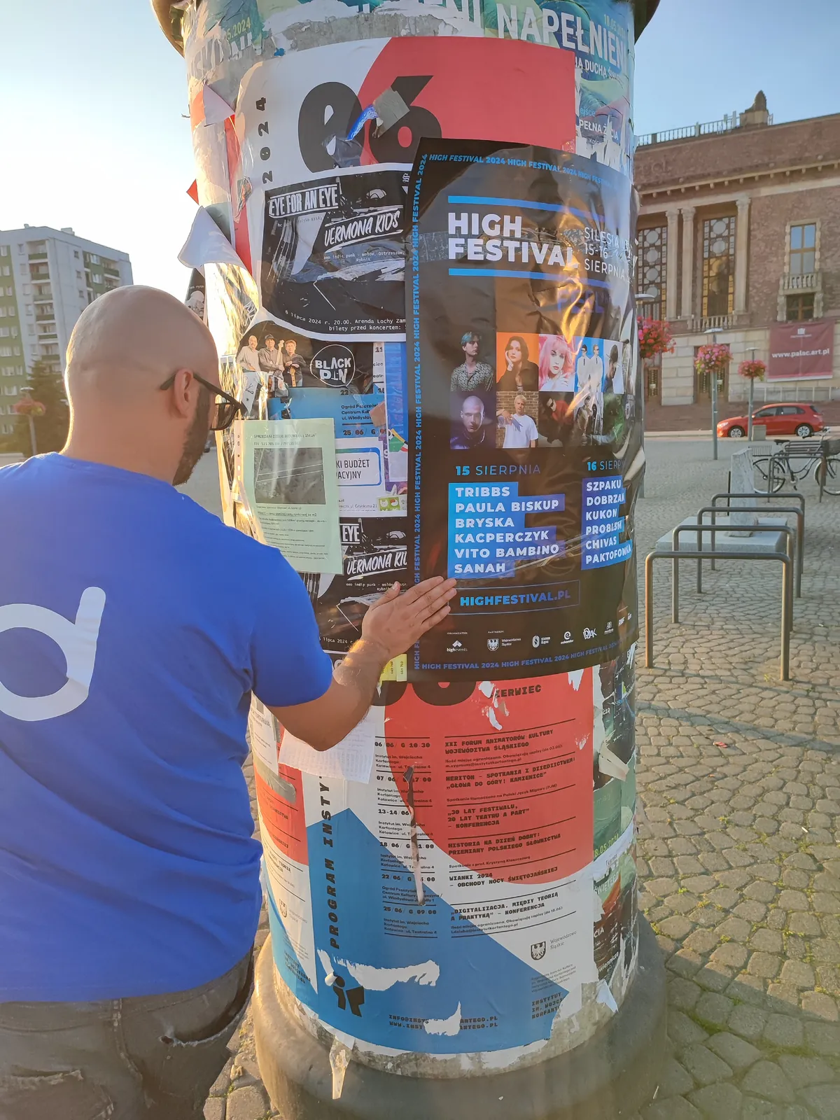 Naklejanie plakatu festiwalu na słupie ogłoszeniowym