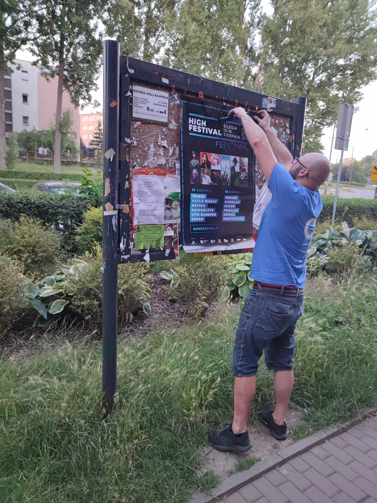 Naklejanie plakatu na tablicy ogłoszeń na skwerze