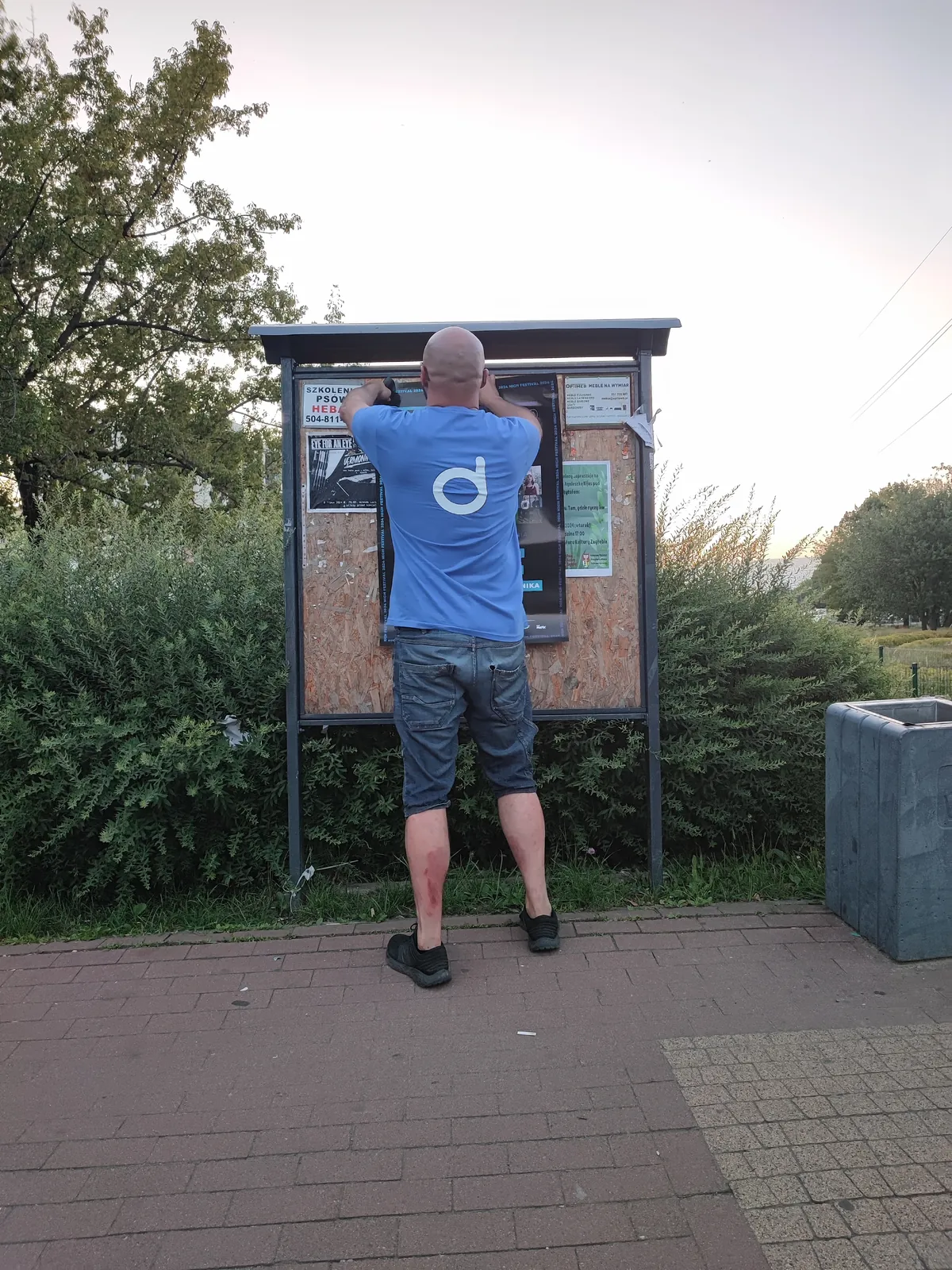 Rozwieszanie plakatu na tablicy przy chodniku